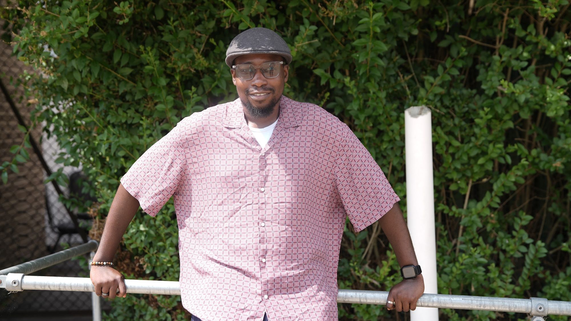 Muheez leaning on a rail against a hedge