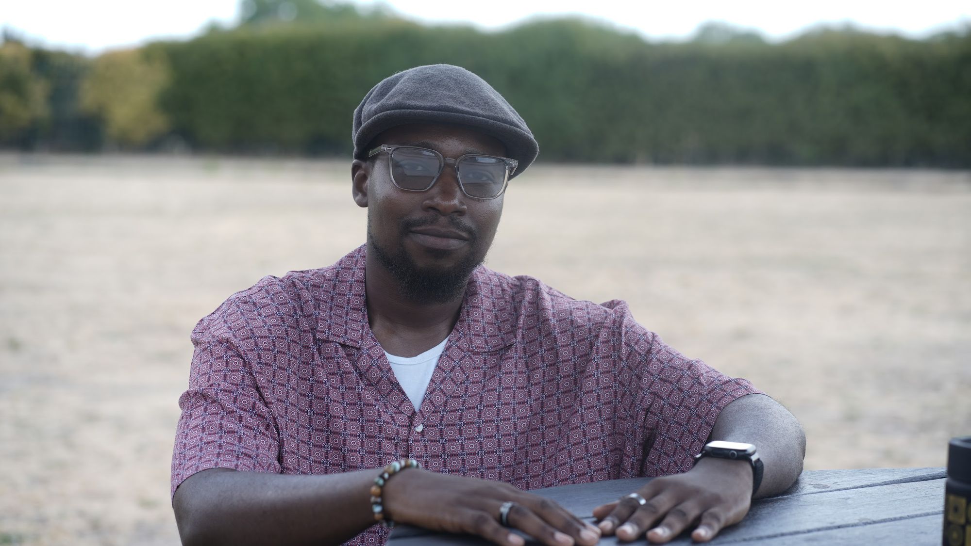 Muheez seated at an outdoor table in a flat cap