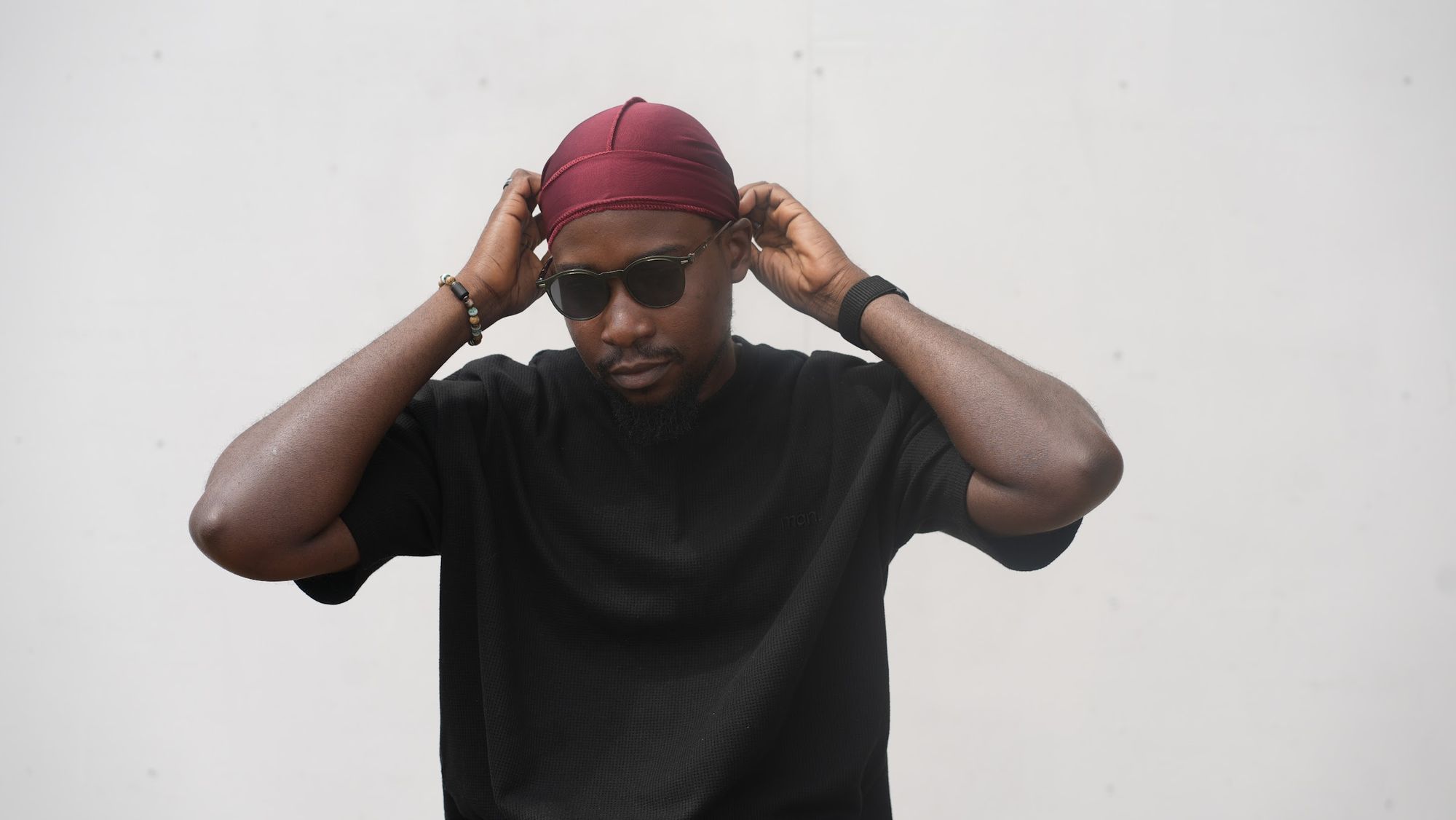 Muheez adjusting a burgundy durag against a pale wall