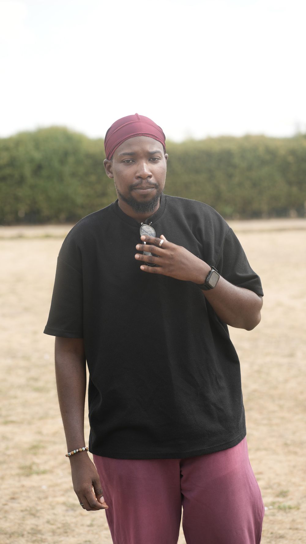 Muheez standing outdoors in a black tee, hand at his chest