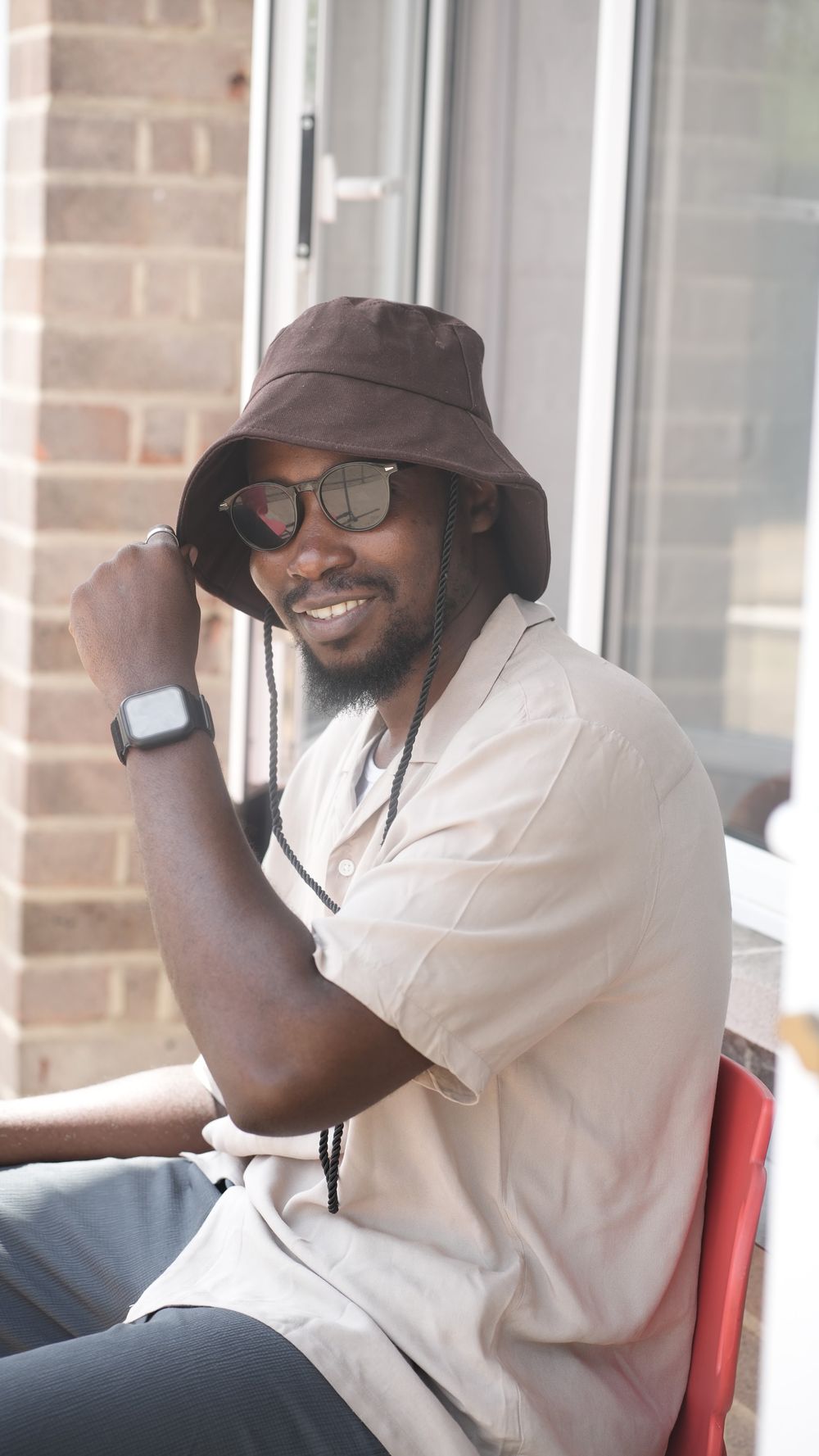 Muheez smiling, seated by a window in a bucket hat